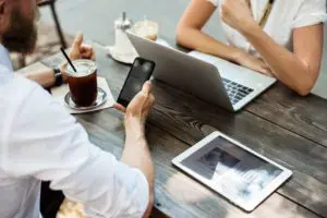 A group of people sitting at a table with laptops and cell phones.