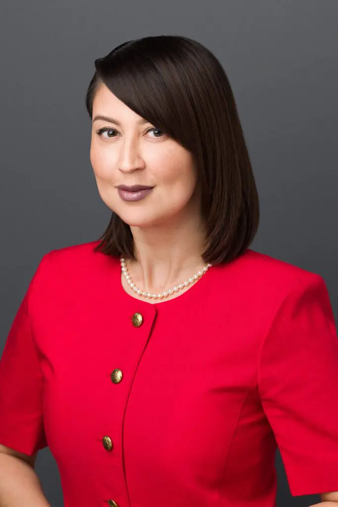 A woman in red jacket standing next to wall.