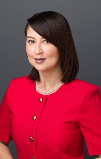 A woman in red jacket standing next to wall.