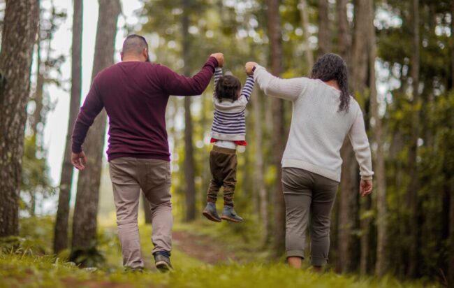 Family walking in forest, holding child's hands.