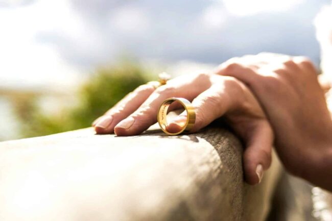 Hand wearing ring resting on wooden surface.