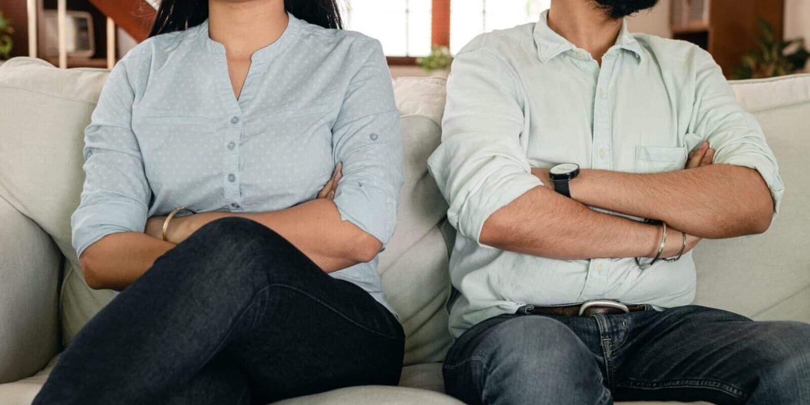 Couple sitting on couch with crossed arms.