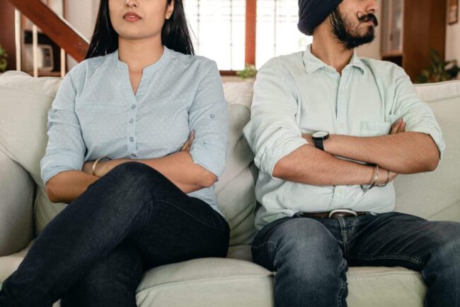 Couple sitting on couch with crossed arms.