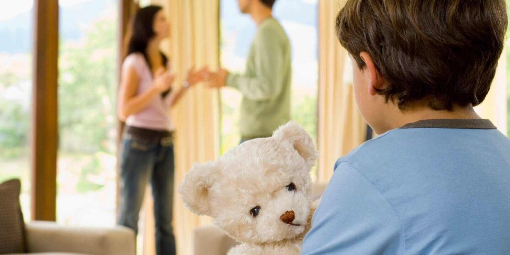 A boy holding a teddy bear in front of two people.