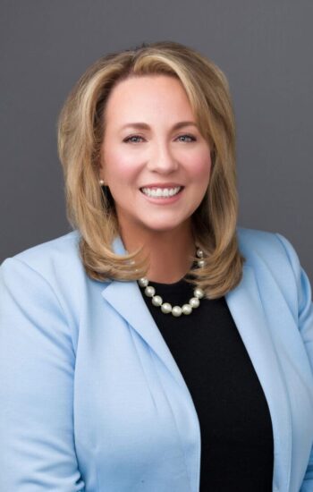 Woman in blue blazer with pearl necklace.