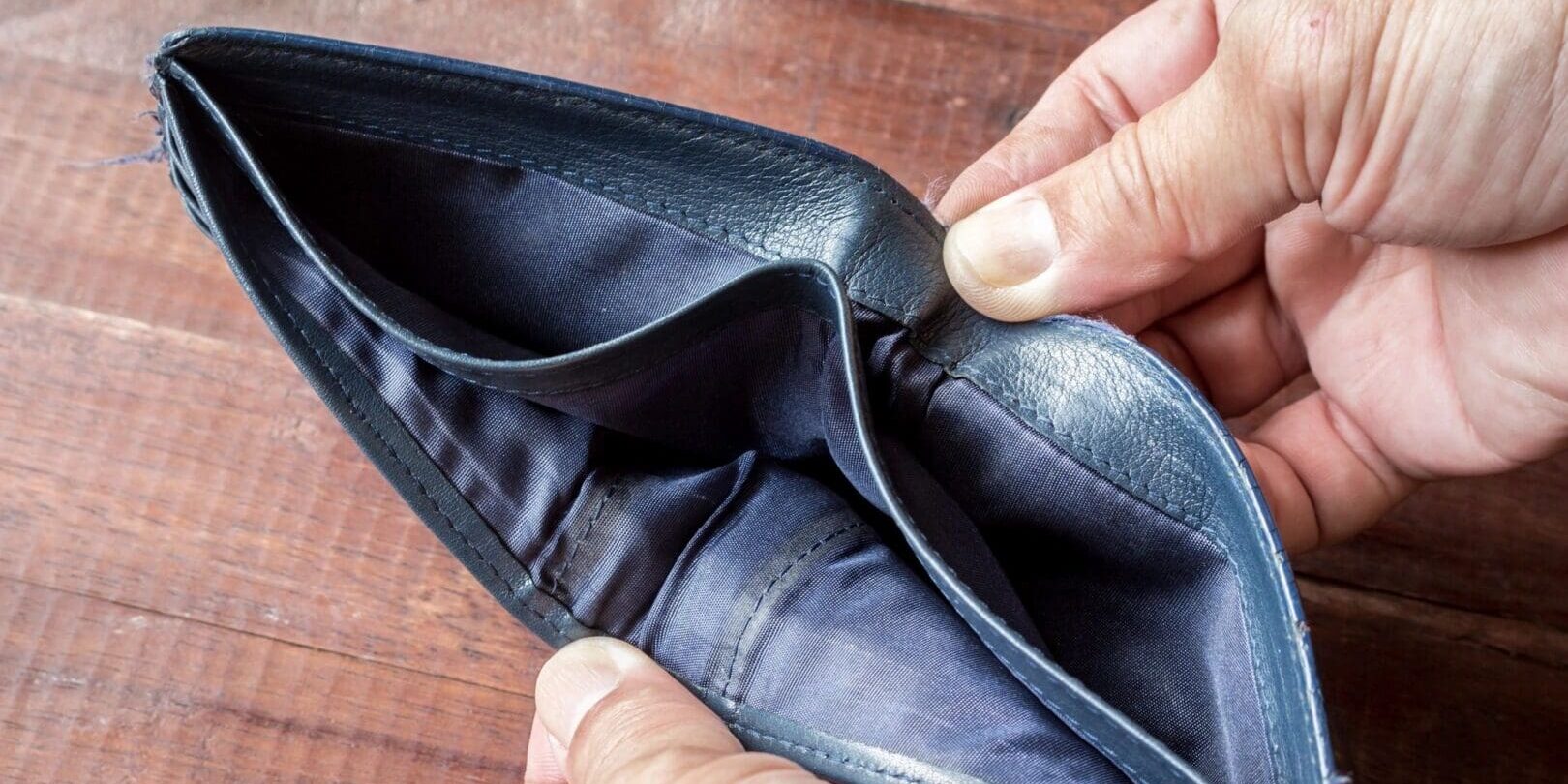 A person holding an empty wallet open on the table.