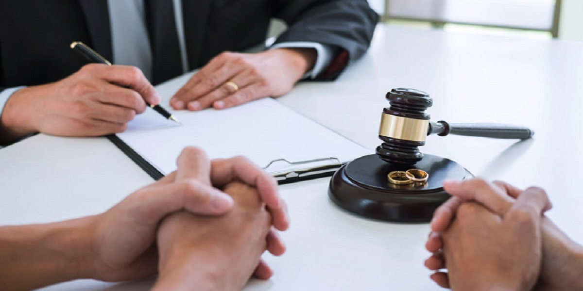 Divorce attorney meeting with couple in Las Vegas, legal documents, gavel, and wedding rings on desk.