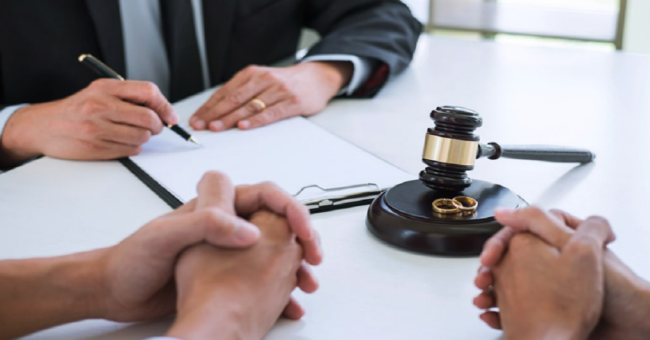 Divorce attorney meeting with couple in Las Vegas, legal documents, gavel, and wedding rings on desk.