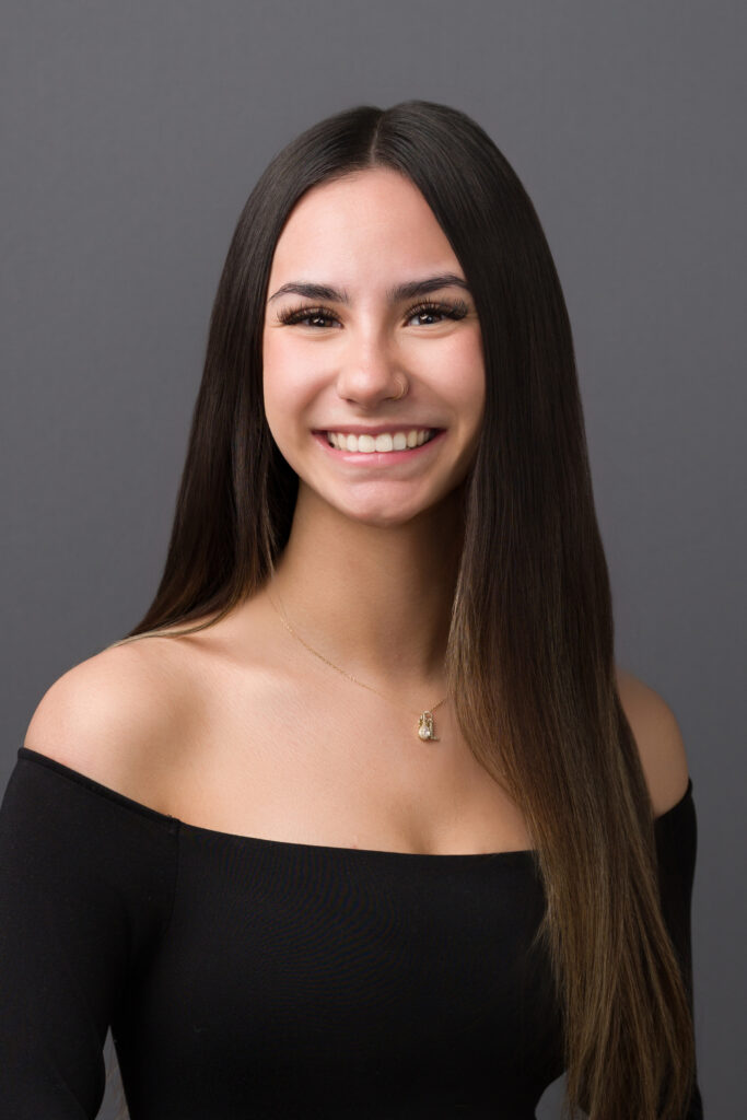 Smiling young woman with long straight hair in black off-shoulder top.