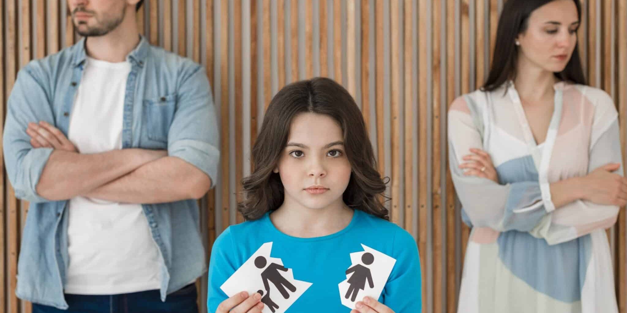 Sad child holding torn paper with parents' symbols, standing between separated mother and father after divorce.
