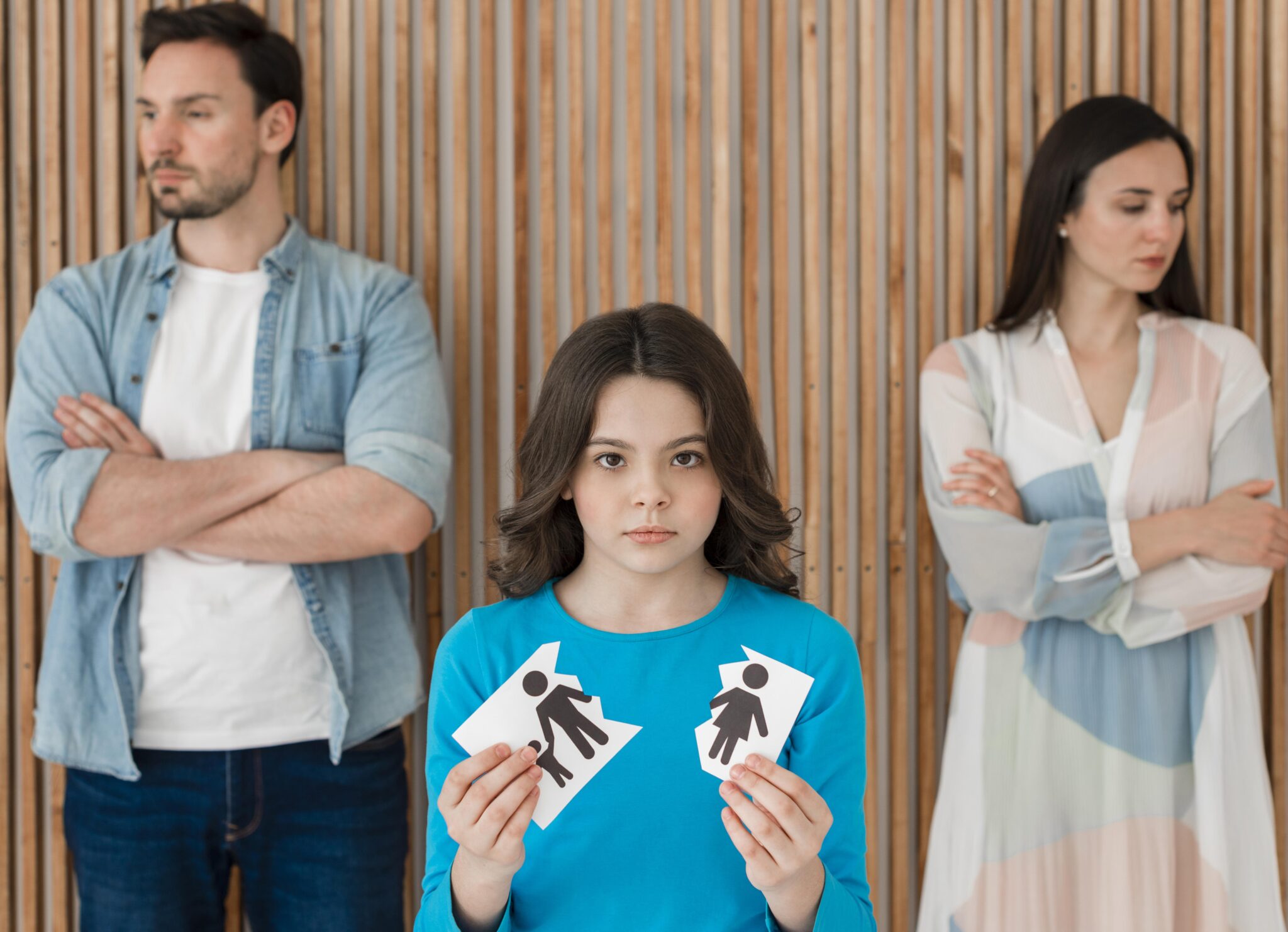 Sad child holding torn paper with parents' symbols, standing between separated mother and father after divorce.
